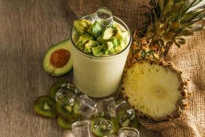 kiwi y piña malteada servido en desechable vaso con hielo cubo aislado en mesa lado ver de sano Mañana Leche sacudir bebida foto