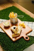 Classic Cajun Beef Double Cheese wrap roll filled with tomato, onion, cucumber with french fries, mayo dip served on wooden board top view of fastfood appetizer photo