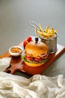 Smoky Double Chicken burger include cheese slice, tomato, onion and lettuce leaf served on wooden board with dip and french fries bucket isolated on grey background side view of appetizer fast food photo