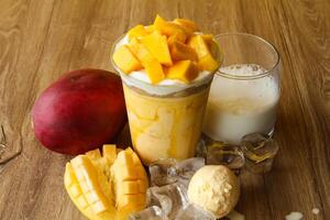 mango malteada con hielo crema cucharón y hielo cubo servido en desechable vaso con hielo cubo aislado en mesa lado ver de sano Mañana Leche sacudir bebida foto