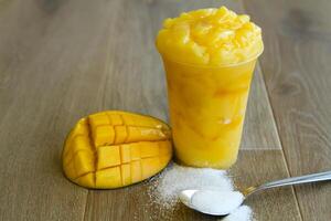 Mango smoothie with sugar spoon served in disposable glass isolated on table side view of healthy morning smoothie drink photo