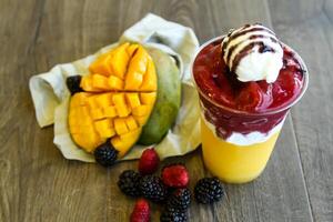 Golden smoothie of mango, strawberry and mulberry with ice cream scoop served in disposable glass isolated on table side view of healthy morning smoothie drink photo