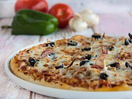 Chicken Tikka Pizza topping with capsicum, mushroom, tomato and olives served in dish isolated on table side view of arabic fastfood photo