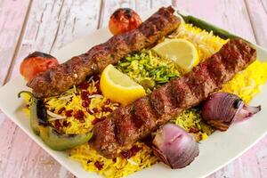 Chelo Kabab Rice topping with pistachio, onion, tomato, lemon slice and pomegranate seeds served in dish isolated on table closeup top vie of arabic spicy food photo