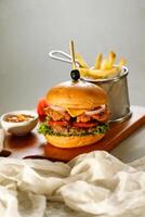 Smoky Double Chicken burger include cheese slice, tomato, onion and lettuce leaf served on wooden board with dip and french fries bucket isolated on grey background side view of appetizer fast food photo