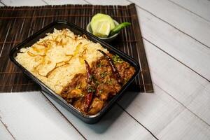 Achari chicken pulao biryani rice with cucumber and lemon slice served in dish isolated on wooden table side view closeup of bangladeshi and indian spicy lunch food photo