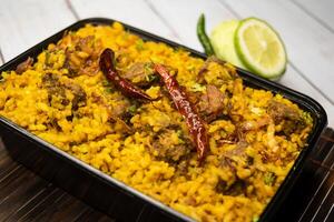 Achari beef khichuri biryani rice pulao with cucumber and lemon slice served in dish isolated on wooden table side view of bangladeshi and indian spices lunch food photo