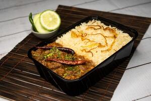 Achari beef pulao biryani rice with cucumber and lemon slice served in dish isolated on wooden table side view of bangladeshi and indian spices food photo