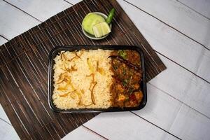Achari chicken pulao biryani rice with cucumber and lemon slice served in dish isolated on wooden table side view of bangladeshi and indian spicy lunch food photo