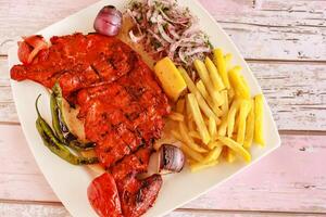 medio A la parrilla tandoori pollo con limón, cebolla y francés papas fritas servido en plato aislado de madera mesa parte superior ver de tandoori parrilla barbacoa comida foto