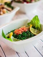 TABOULEH Salad with tomato, green herb leaves and lemon served in dish isolated on wooden table top view of cold mazza arabic food photo