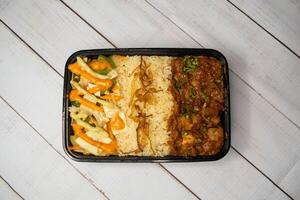 Chicken Bhuna with pulao biryani rice with cucumber, dip sauce and lemon slice served in dish isolated on wooden table top view of bangladeshi and indian spicy lunch food photo