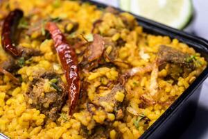 Achari beef khichuri biryani rice pulao with cucumber and lemon slice served in dish isolated on wooden table closeup side view of bangladeshi and indian spicy food photo