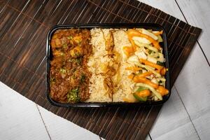 Chicken Bhuna with pulao biryani rice with cucumber, dip sauce and lemon slice served in dish isolated on wooden table top view closeup of bangladeshi and indian spicy lunch food photo