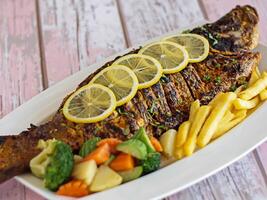 A la parrilla hamour pescado con salsa, limón rebanada y tomate servido en plato aislado en mesa de cerca parte superior ver de A la parrilla Mariscos foto