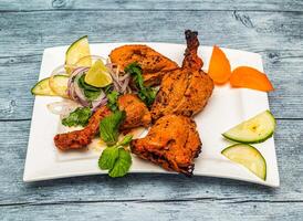 Grilled tandoori chicken with lemon and onion served in dish isolated on wooden table top view of indian spicy food photo