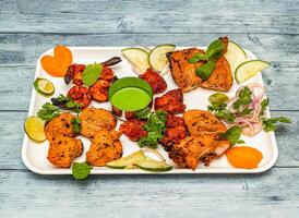 tandoori platter with tandoori chicken , tikka kabab, and grilled prawn with onion and lemon served in dish isolated on wooden table top view of indian spicy food photo