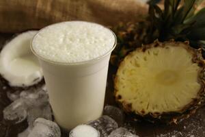 piña colada con piña, plátano y Leche servido en desechable vaso aislado en mesa lado ver de sano bebida foto