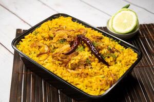 Achari chicken khichuri biryani rice pulao with cucumber and lemon slice served in dish isolated on wooden table side view of bangladeshi and indian spices lunch food photo