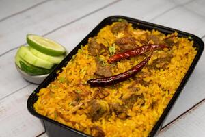 Achari beef khichuri biryani rice pulao with cucumber and lemon slice served in dish isolated on wooden table side view of bangladeshi and indian spicy lunch food photo