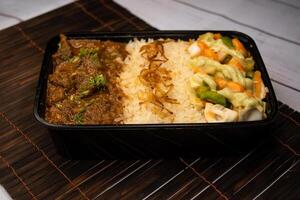 Beef Bhuna with pulao biryani rice with cucumber, dip sauce and lemon slice served in dish isolated on wooden table side view of bangladeshi and indian spicy lunch food photo