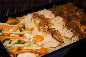 Chicken Bhuna with pulao biryani rice with cucumber, dip sauce and lemon slice served in dish isolated on wooden table side view closeup of bangladeshi and indian spices food photo