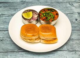 chicken pav bhaji or vada pav bun kabab with lemon and onion served in dish isolated on wooden table top view of indian spicy food photo