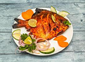 tandoori pomfret fish fry with lemon and onion served in dish isolated on wooden table top view of indian spicy food photo