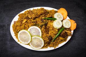 carne de vaca yakhni Biryani arroz pulao con pepino, Lima rebanada y Zanahoria servido en plato aislado en oscuro antecedentes parte superior ver indio especias, bangladeshi y pakistaní comida foto