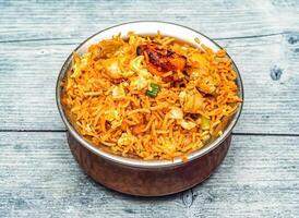 mixed non veg fried rice or chicken and shrimp biryani served in copper dish isolated on wooden table top view of indian spicy food photo