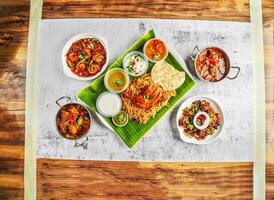 tandoori chicken biryani rice pulao, pepper mutton dry, mutton rogan josh, chicken karahi korma masala, sharimp or parawn masala, salad, chutney, raita and sauce served dish top view of indian food photo