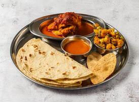 chicken thali set with chicken korma, mixed vegetable of aloo gobi matar, shorba and chapati served in dish isolated on background top view of indian spicy food photo