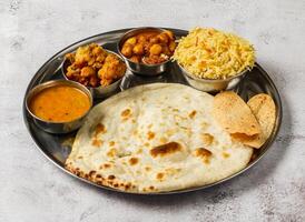 Vegetable thali set with plain biryani, mixed vegetable of aloo gobi matar, chanay, shorba and chapati served in dish isolated on background top view of indian spicy food photo