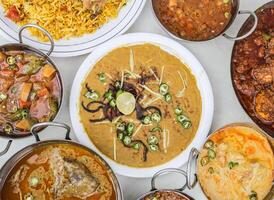 Chicken haleem, chicken karahi, biryani, beef nihari, curry pakora, chanay, aloo shimla mirch and keema isolated on grey background top view of pakistani and assorted indian spices food variety photo