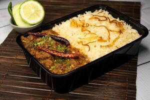 Achari beef pulao biryani rice with cucumber and lemon slice served in dish isolated on wooden table side view closeup of bangladeshi and indian spicy lunch food photo