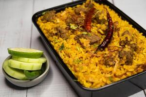 Achari beef khichuri biryani rice pulao with cucumber and lemon slice served in dish isolated on wooden table side view of bangladeshi and indian spicy food photo