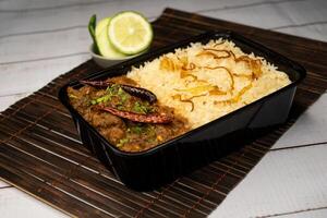 Achari beef pulao biryani rice with cucumber and lemon slice served in dish isolated on wooden table side view of bangladeshi and indian spicy food photo