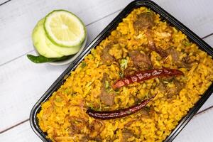 Achari beef khichuri biryani rice pulao with cucumber and lemon slice served in dish isolated on wooden table top view closeup of bangladeshi and indian spicy lunch food photo