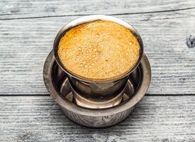 filter coffee served in steel cup isolated on wooden table top view of indian hot drink photo