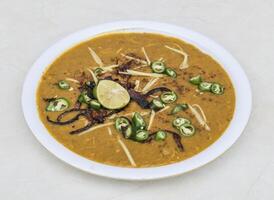 Chicken haleem topping with fried onion, lemon slice and green chilli served in plate isolated on grey background side view of pakistani and indian spices food photo