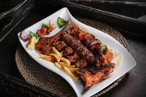 Mix grill with lamb chop, chicken tikka, shish tawook, beef kabab, fries and salad served in dish isolated on red mat top view on table arabic food photo