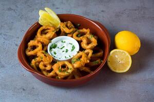 Crispy Baby Calamari Rings with dip and lemon served in dish isolated on grey background top view of bahrain food photo