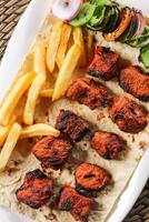 Spicy bbq Chicken Tikka boti kabab with fries and salad served in dish isolated on red mat top view on table arabic food photo