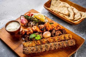 mezcla parrilla con shish tawook, pollo kebab, carne de vaca brocheta, tikka boti, reshmi y malai Agave pan, yaya, tandoori Roti, raita, inmersión y ensalada, tomate cebolla y limón servido en de madera tablero parte superior ver foto