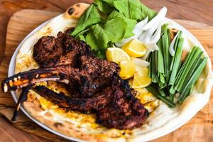 Lamb Chop or mutton chops with red sauce, bahraini bread tandoori nan, lime and salad served in dish isolated on wooden table top view middle eastern grills food photo