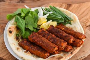 Spicy Chicken kabab meat seekh kebab with bahraini bread tandoori nan, lime and salad served in dish isolated on wooden table top view middle eastern grills food photo