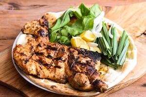 Half Grilled Chicken with bahraini bread tandoori nan, lime and salad served in dish isolated on wooden table top view middle eastern grills food photo