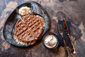 Marble Chocolate Waffle with chocolate, whipped cream, knife and fork served in dish isolated on dark background top view cafe dessert food photo