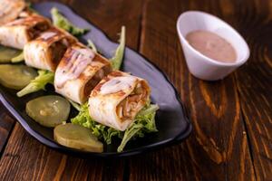 Quesadilla chicken wraps with cucumber, lettuce leaves and mayonnaise dip served in dish isolated on wooden table side view of arabic food photo