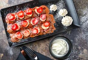 Strawberry and Banana poffers with chocolate, whipped cream, knife and fork served in dish isolated on dark background closeup top view of cafe baked dessert food photo